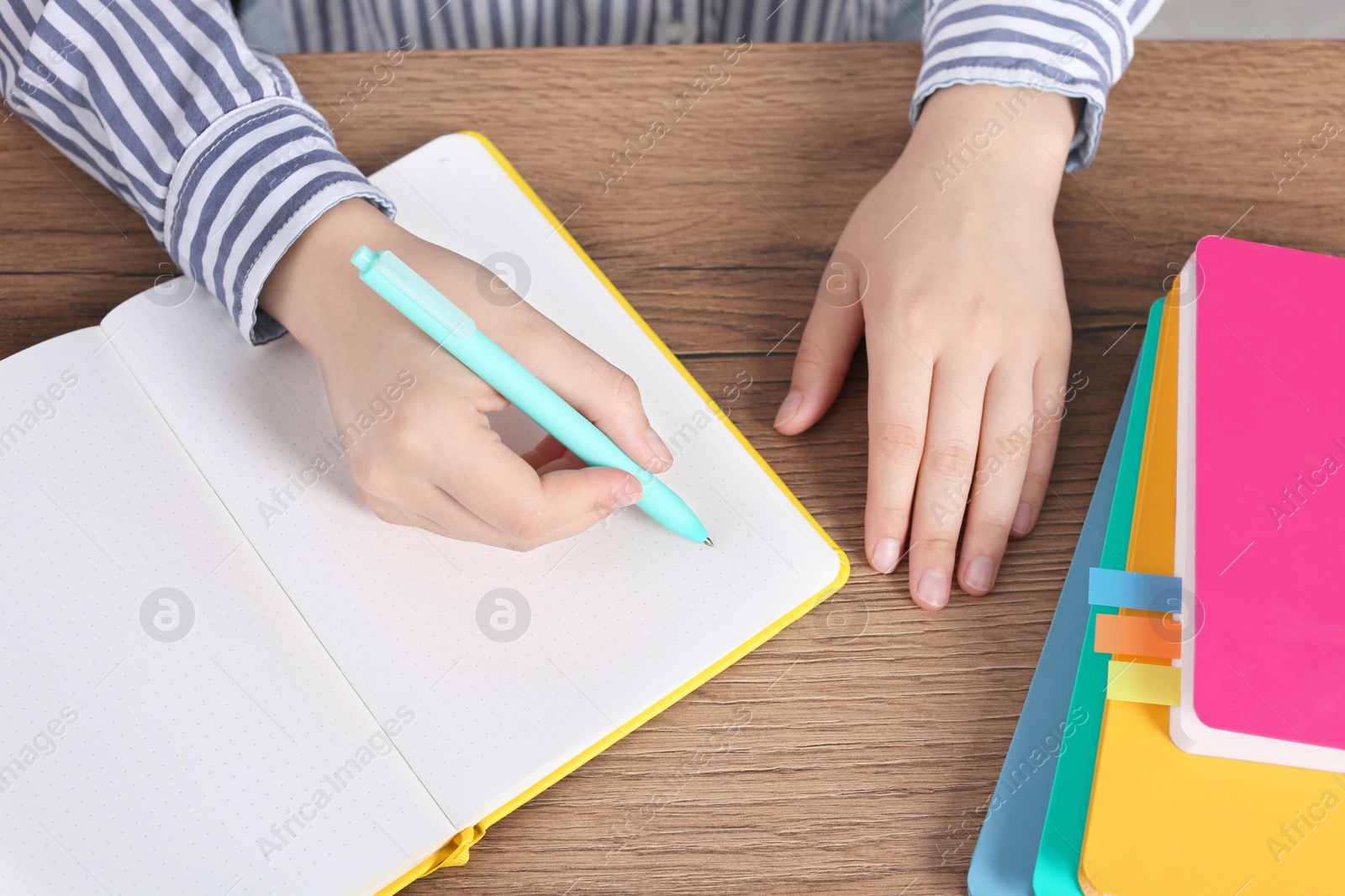 Photo of Woman writing in notebook at wooden table, above view