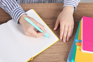 Woman writing in notebook at wooden table, above view