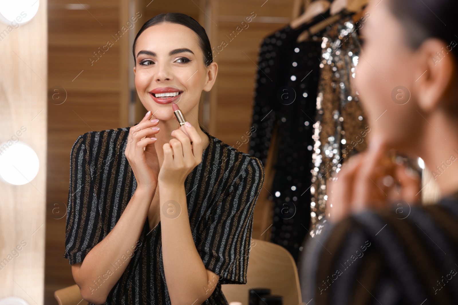 Photo of Bright makeup. Beautiful woman applying lipstick near mirror in dressing room