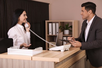 Receptionist talking on phone while working with client at countertop in office