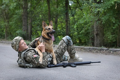 Man in military uniform with German shepherd dog lying on road