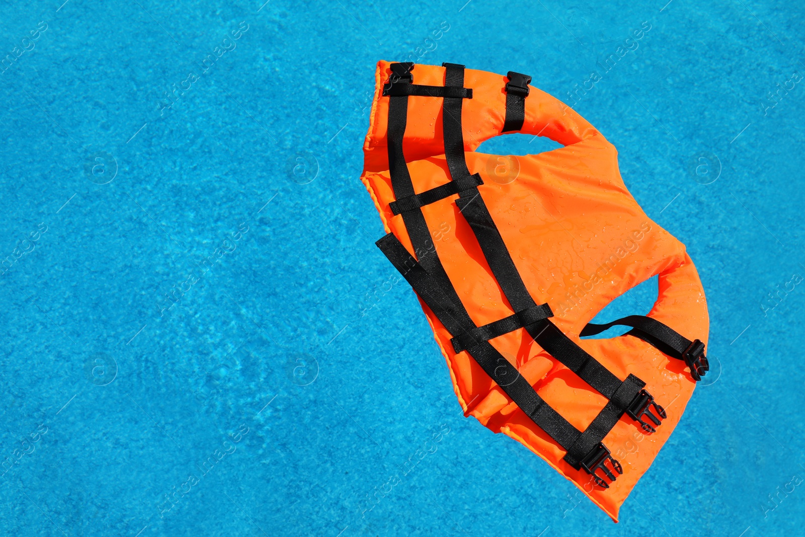 Photo of Bright orange life jacket floating in swimming pool, top view