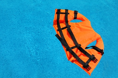 Photo of Bright orange life jacket floating in swimming pool, top view