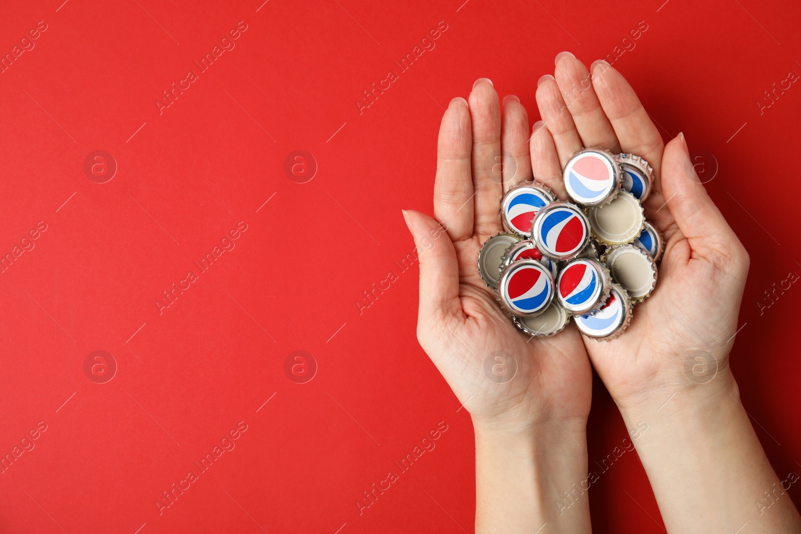 Photo of MYKOLAIV, UKRAINE - FEBRUARY 12, 2021: Woman holding Pepsi lids on red background, top view. Space for text