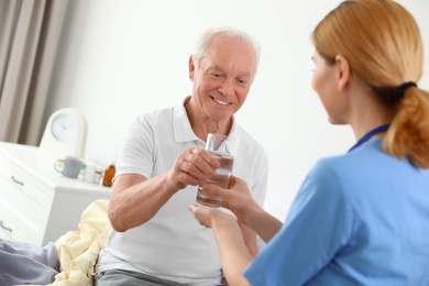 Photo of Nurse giving glass of water to elderly man indoors. Medical assistance