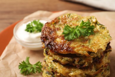 Delicious zucchini pancakes and bowl with sour cream on table, closeup