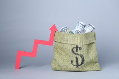 Photo of Economic profit. Money bag with banknotes and arrow on light grey background