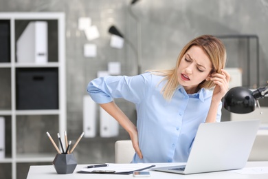 Photo of Young woman suffering from back pain in office