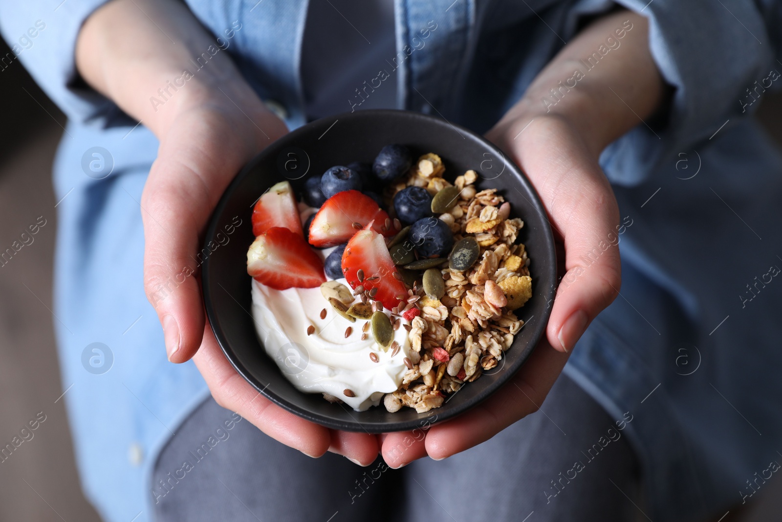 Photo of Woman holding bowl of tasty granola with berries, yogurt and seeds, top view