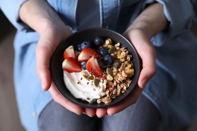 Photo of Woman holding bowl of tasty granola with berries, yogurt and seeds, top view