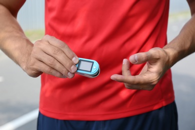 Young man checking pulse with medical device after training, closeup