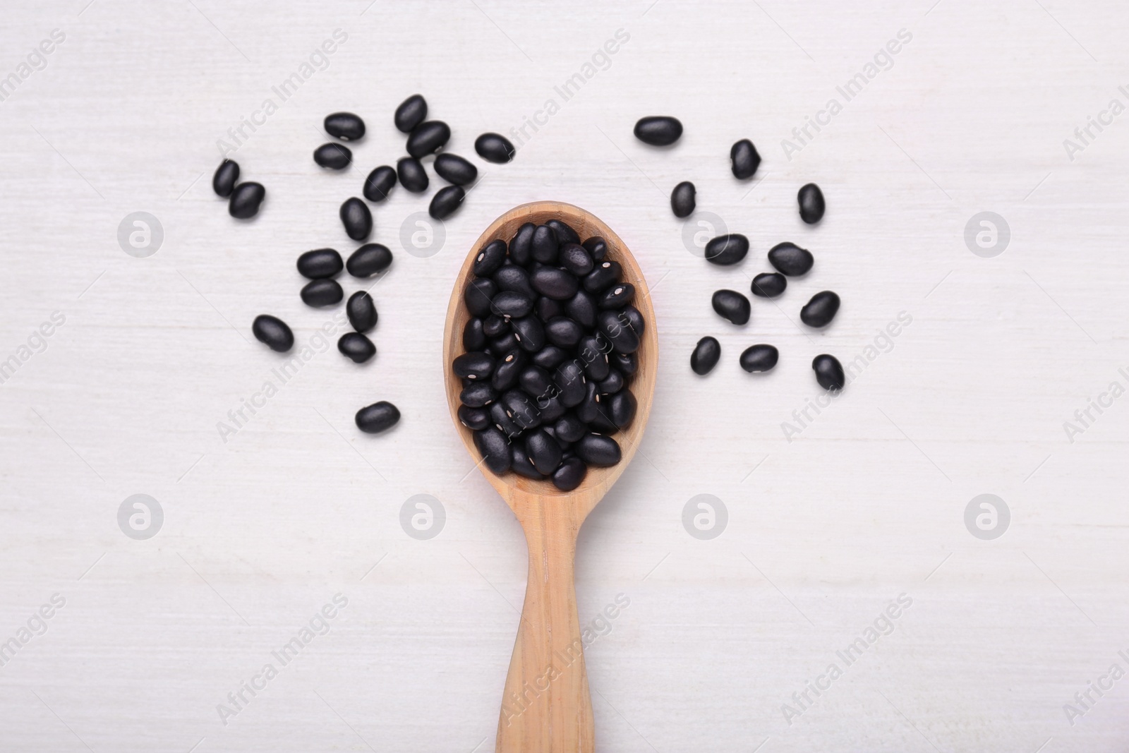 Photo of Spoon of raw black beans on white wooden table, top view