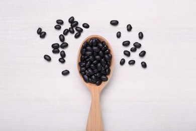 Spoon of raw black beans on white wooden table, top view