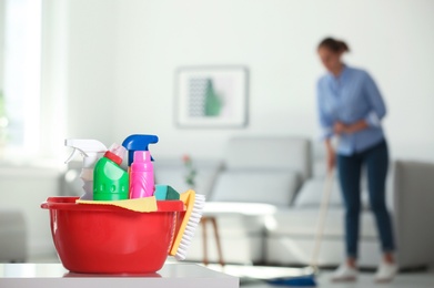 Basin with cleaning supplies and blurred woman on background