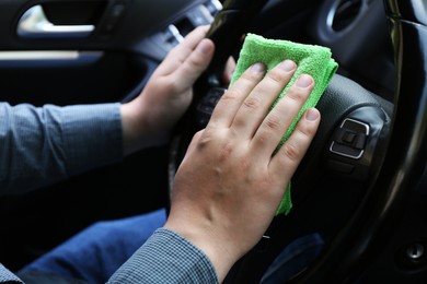 Man cleaning steering wheel with rag in car, closeup