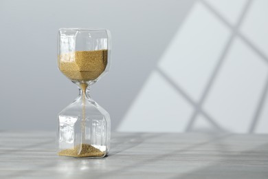 Photo of Hourglass with flowing gold sand on table against white wall, space for text