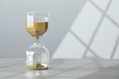 Hourglass with flowing gold sand on table against white wall, space for text