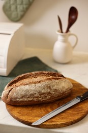 Photo of Wooden bread basket and freshly baked loaf on white marble table in kitchen