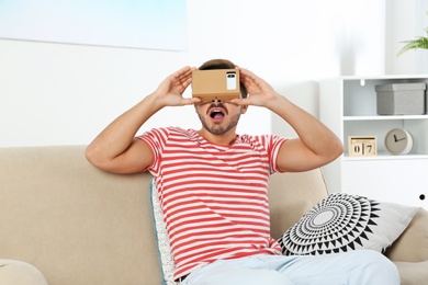 Young man using cardboard virtual reality headset at home