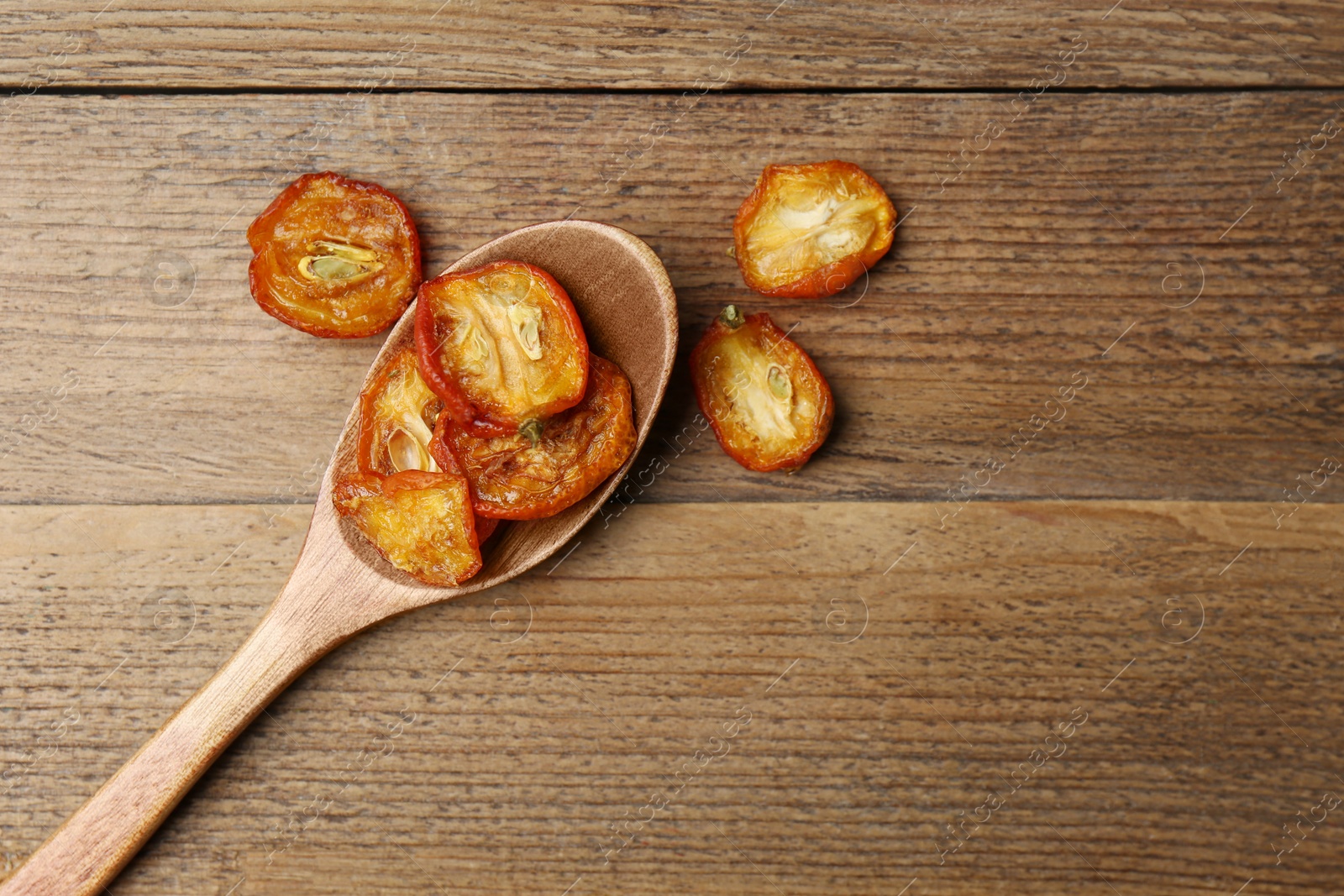 Photo of Spoon and cut dried kumquat fruits on wooden table, flat lay. Space for text