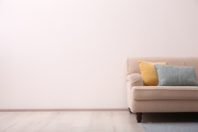 Photo of Comfortable beige sofa near light wall indoors, space for text. Simple interior