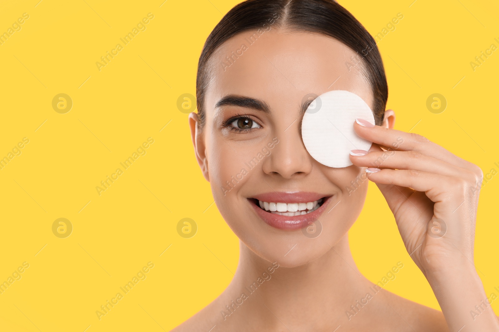 Photo of Beautiful woman removing makeup with cotton pad on yellow background. Space for text