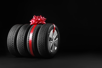 Photo of Gift set of wheels with winter tires on black background, space for text