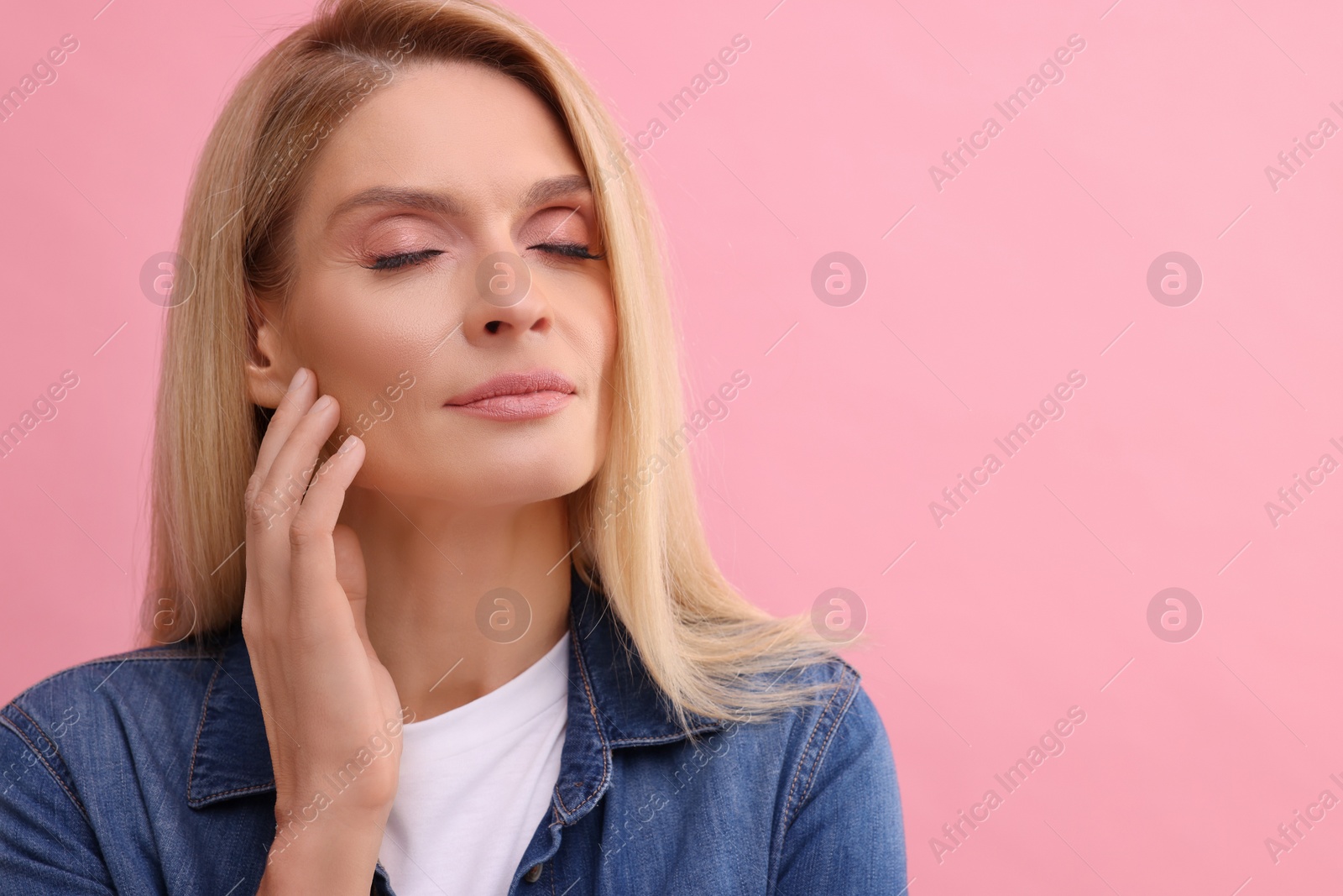 Photo of Portrait of beautiful middle aged woman with blonde hair on pink background. Space for text