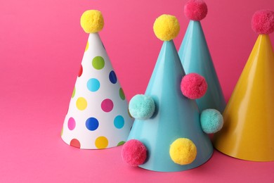 Photo of Beautiful party hats with pompoms on pink background
