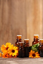 Bottles with essential oils, mint and flowers on wooden table. Space for text