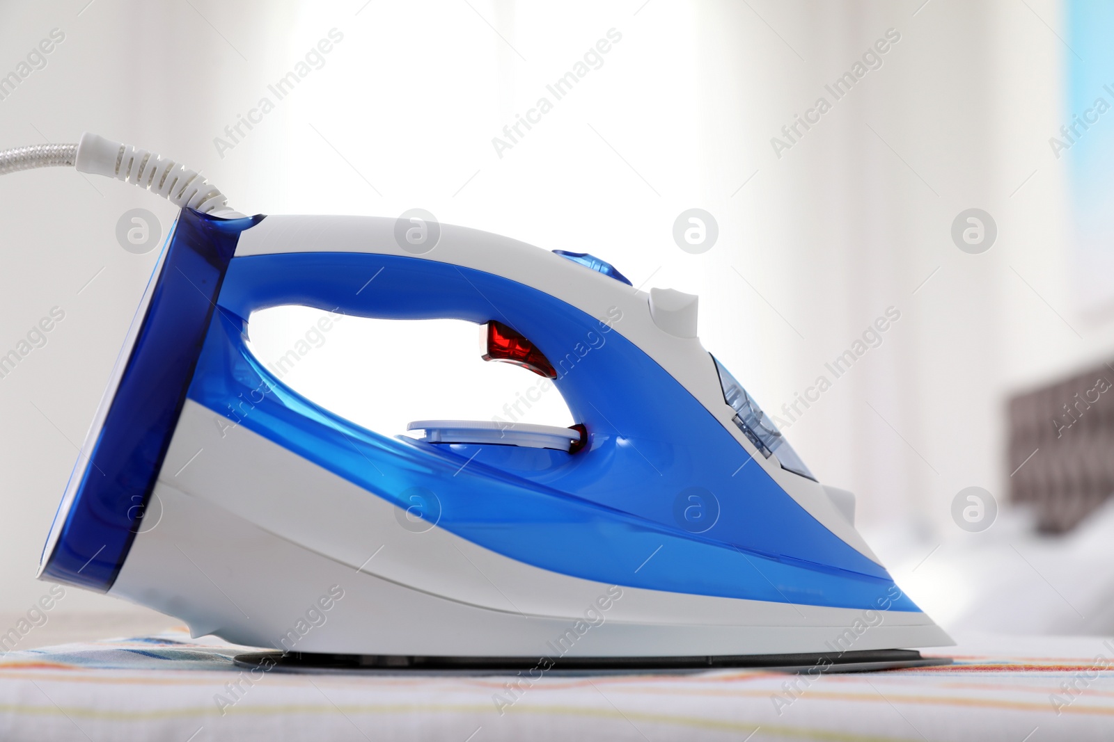 Photo of Modern electric iron on board indoors. Household appliance