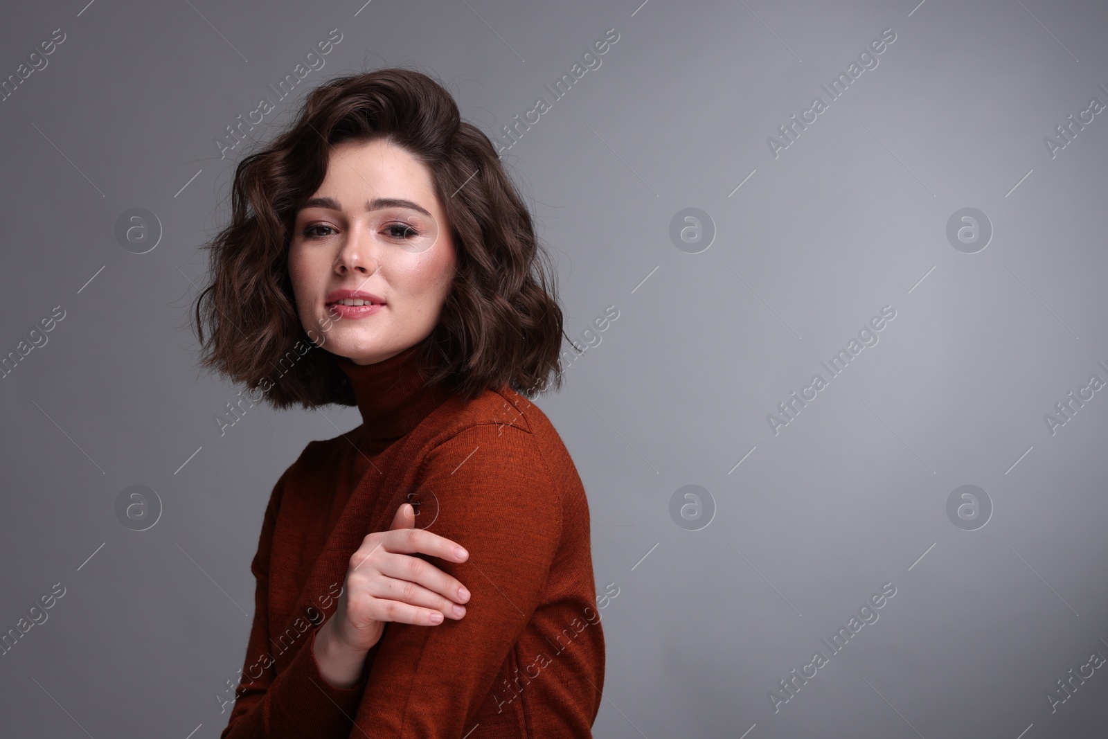 Photo of Portrait of beautiful young woman with wavy hairstyle on grey background. Space for text