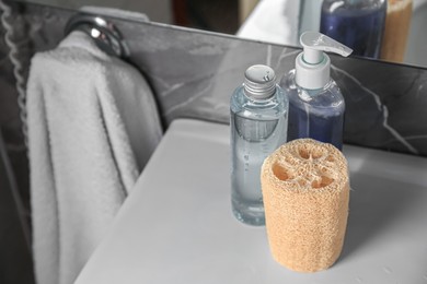 Natural loofah sponge and shower gel bottles on washbasin in bathroom. Space for text