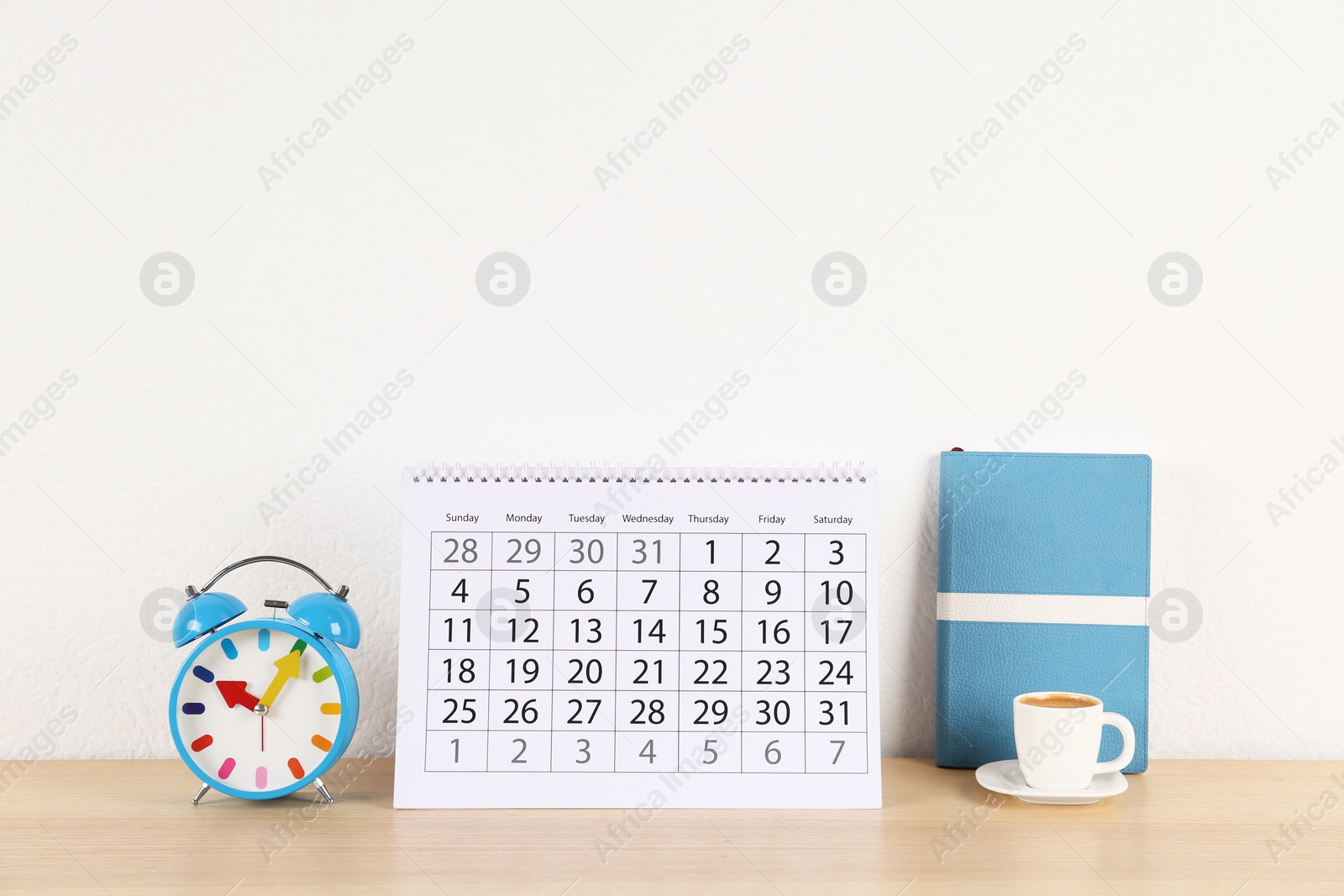 Photo of Calendar, alarm clock and cup of coffee on wooden table