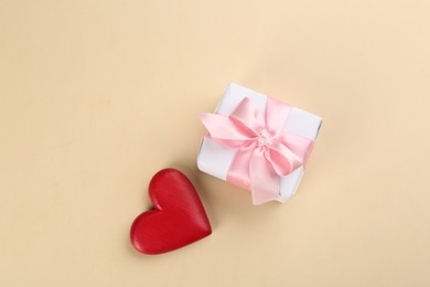 Beautiful gift box and red heart on beige background, flat lay. Valentine's day celebration