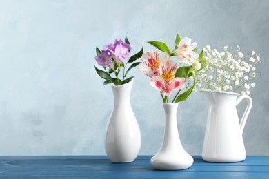 Photo of Different beautiful flowers in vases on wooden table against light blue background, space for text