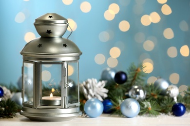Christmas lantern with burning candle and festive decor on white table against blurred lights