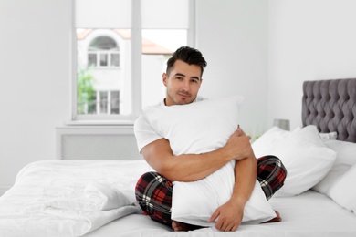 Photo of Young man with soft pillow on bed at home