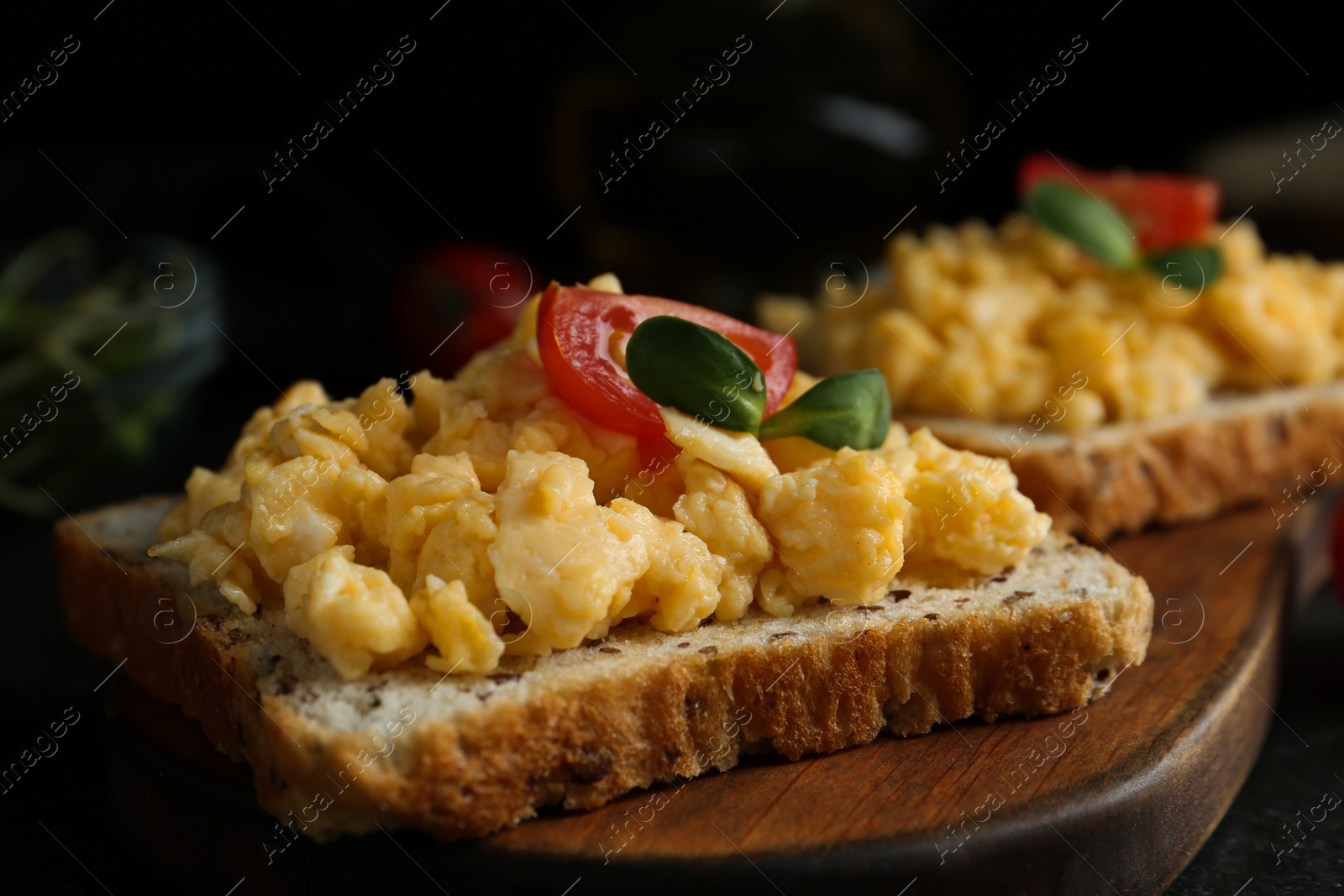 Photo of Tasty scrambled egg sandwiches served on wooden board, closeup