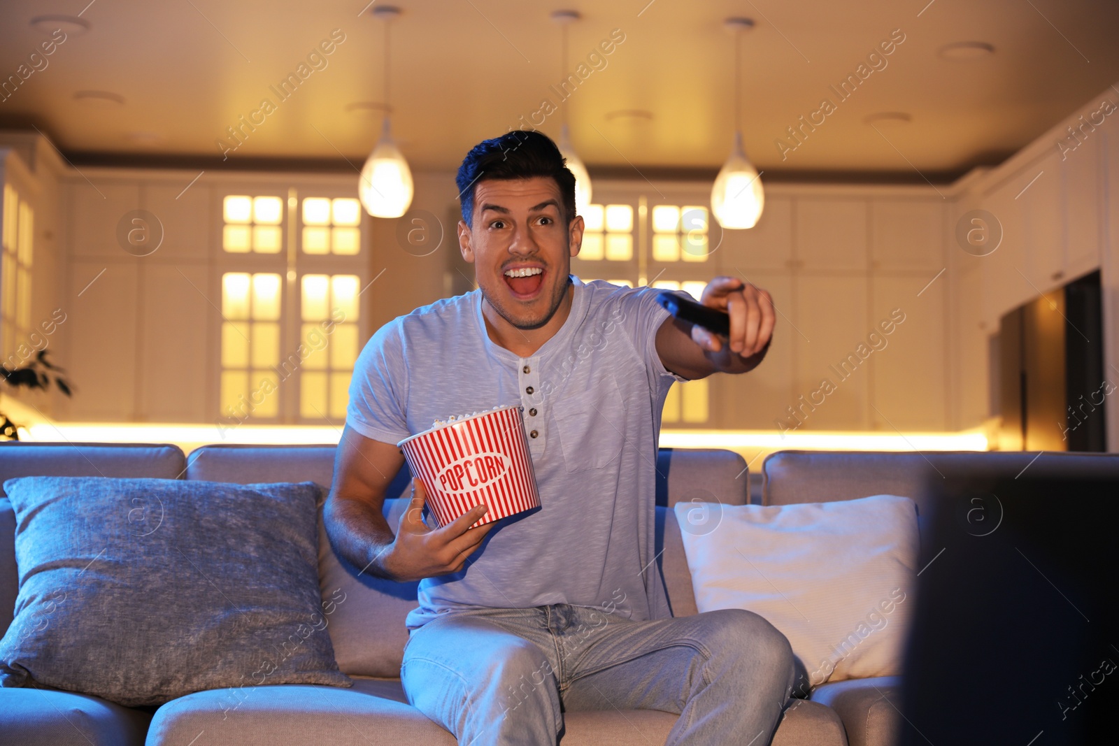 Photo of Man watching movie with popcorn on sofa at night