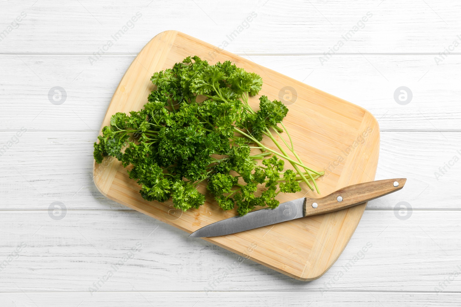 Photo of Fresh curly parsley, cutting board and knife on white wooden table, top view