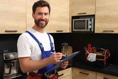 Photo of Professional plumber with clipboard and tool belt in kitchen