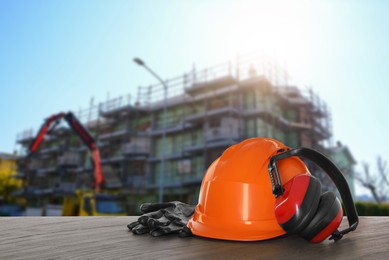 Image of Safety equipment. Hard hat, gloves and protective headphones on wooden surface near unfinished building outdoors, space for text