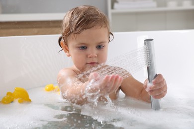 Photo of Cute little girl playing with shower head in bathtub at home