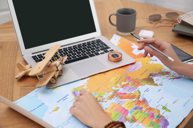 Woman with world map and laptop planning trip at wooden table, closeup