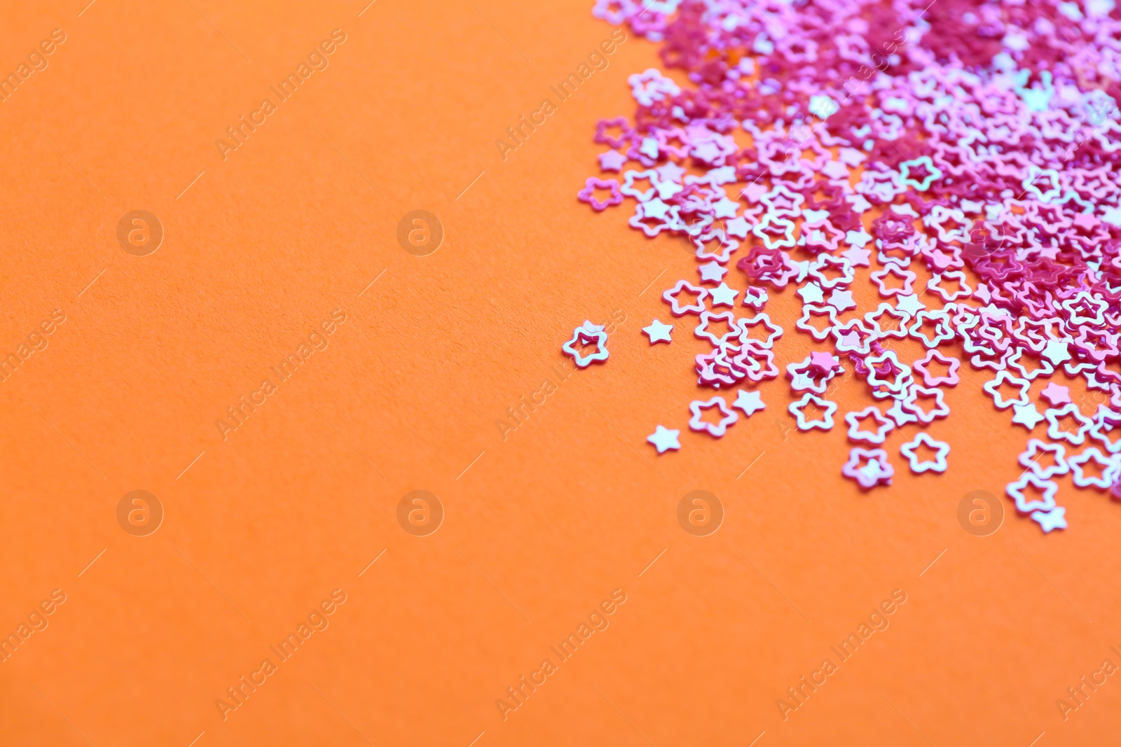 Photo of Shiny bright star shaped glitter on pale coral background. Space for text