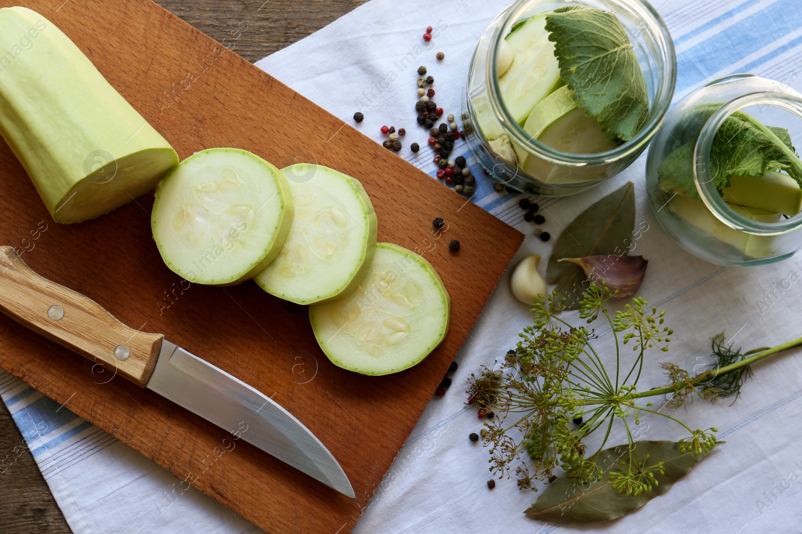 Photo of Cut fresh zucchini, other ingredients and glass jars on wooden table, flat lay. Pickling vegetables