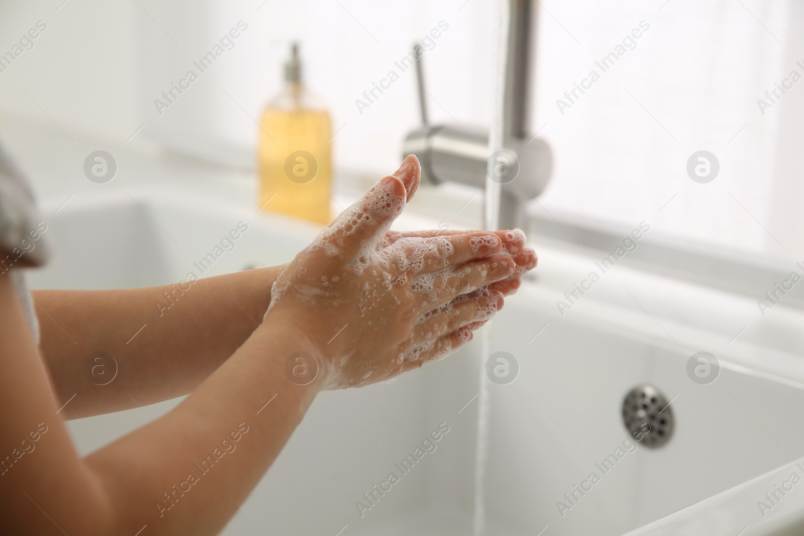 Photo of Little girl washing hands with liquid soap at home, closeup