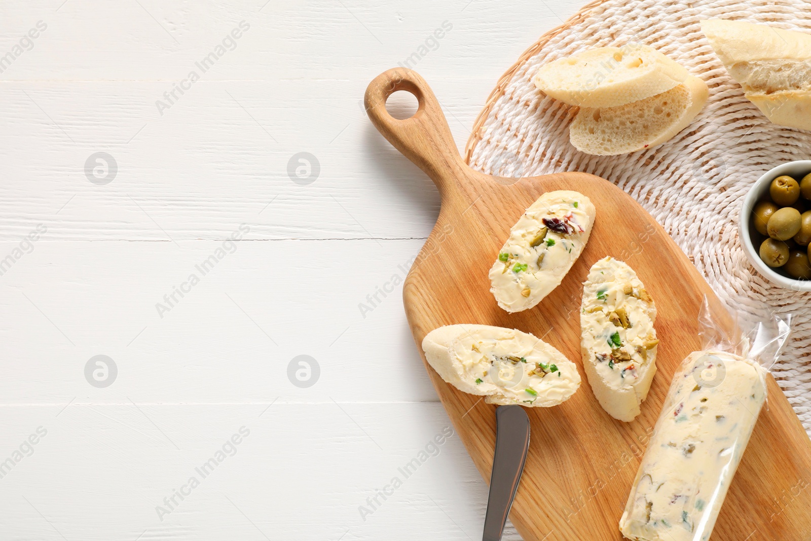 Photo of Tasty butter with olives, green onion and bread on white wooden table, top view. Space for text