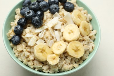 Photo of Tasty oatmeal with banana, blueberries, coconut flakes and honey served in bowl on beige table, closeup